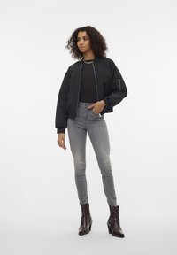 Czarna kurtka bomberka z zamkiem błyskawicznym z przodu, dopasowanymi mankietami i bocznymi kieszeniami, noszona na czarnym topie; w połączeniu z szarymi obcisłymi dżinsami i brązowymi botkami za kostkę.