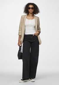 Beige Blazer, weißes knöpfbares Tanktop, schwarze weit geschnittene Jeans und schwarze Sneaker mit weißen Sohlen; accessoriert mit einer Schildpatt-Sonnenbrille und einer Handtasche.