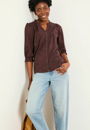 Burgundy button-up blouse with floral texture, gathered sleeves, and a v-neckline. Paired with light blue straight-leg jeans.