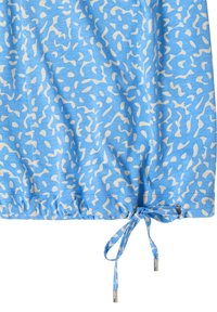 Tissu bleu clair avec un motif abstrait blanc. Comprend un cordon de serrage élastique à l'ourlet avec des cordons assortis et des accents argentés.