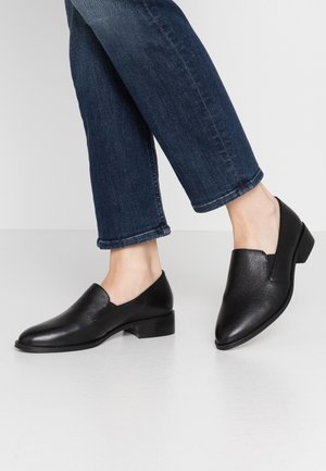 Sorte læder slip-on sko med spids tå, struktureret overflade, lav blokhæls og elastisk indsats i siderne. Bæres med opsmøgede mørke jeans.