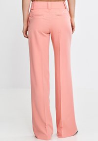 Jasnoróżowe spodnie szerokie wykonane z gładkiego materiału, z tylnymi kieszeniami i dopasowanym krojem. Spodnie mają czysty, minimalistyczny design.