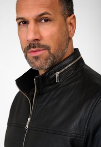 Black leather jacket with a high collar, silver zipper detailing, and a smooth texture. Features seam accents on the front.