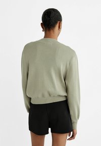 Pull en rib (côtelé) vert clair avec un col rond et des poignets ajustés, associé à un short noir. La texture semble douce et légère.