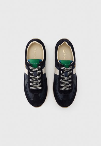 Pereche de adidași casual bleumarin și albi cu șireturi cu model, etichetă verde pe limbă și interior bej, priviți de sus pe fundal alb.