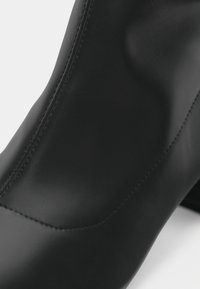 Gros plan d'une chaussure en cuir noir élégante avec des coutures détaillées et une texture lisse sur fond blanc.