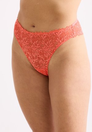 Female torso wearing coral pink high-cut lace underwear with floral pattern and scalloped edges against a plain background.