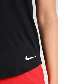Nike svart atletisk linne med slim fit, slät textur och en välkänd vit logotyp på den nedre sid sömmen. Kombinerat med röda shorts.