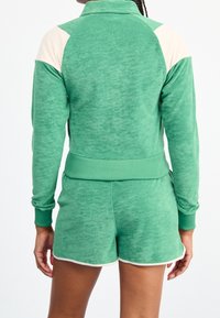 Grön fleece-träningsdräkt med en zipjacka med ribbade ärmslut och midja. Shortsen är i matchande grönt med vita detaljer.