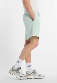 Pantalones cortos de color verde menta claro con cinturilla elástica y bolsillos laterales, combinados con calcetines tobilleros blancos y zapatillas gris y blancas.