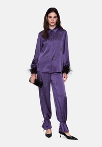 Purple satin pajama set with embroidered designs, feather accents at cuffs, and drawstring ankles. Paired with black clutch and heels.