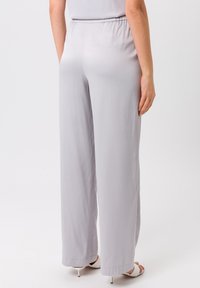 Pantalons larges gris clair en tissu lisse avec une taille élastique. Présente une coupe décontractée et un léger éclat.