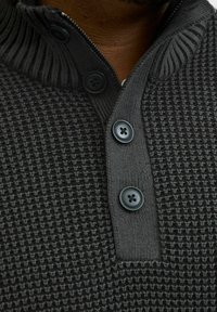 Dark gray textured sweater with a high collar, half-zip, and three black buttons. Ribbed detailing on the collar and cuffs.