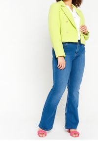 Jasně zelené texturované zkrácené sako s dvojitými knoflíky, nošené přes bílé blůzky. V kombinaci s modrými rozšířenými džíny a růžovými sandály na podpatku.