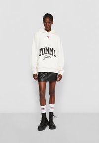 Felpa con cappuccio crema con "TOMMY Jeans" in bold nero, abbinata a una mini gonna in pelle nera e stivali da combattimento neri con lacci.