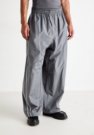 Gray waterproof pants with an elastic waistband, featuring white side stripes and a relaxed fit. Worn with black sturdy boots.