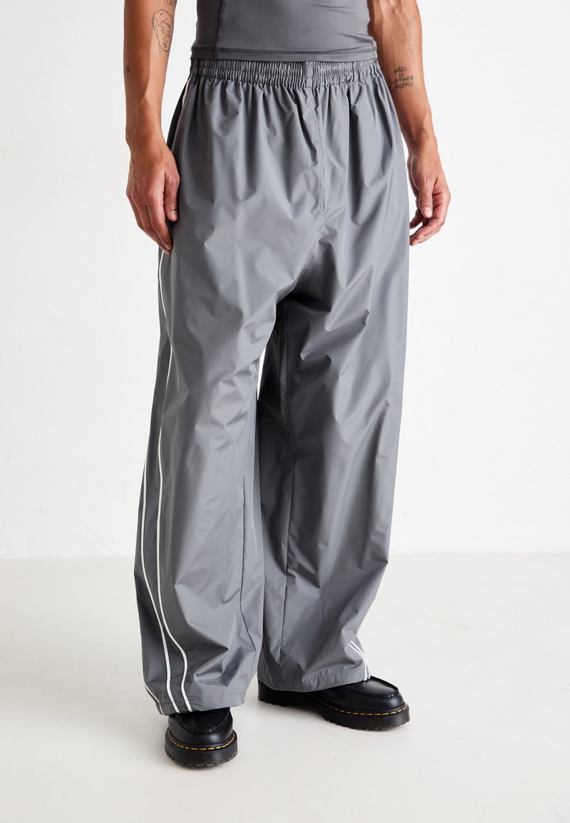 Gray waterproof pants with an elastic waistband, featuring white side stripes and a relaxed fit. Worn with black sturdy boots.