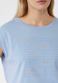 Himmelblaues T-Shirt mit kurzen Ärmeln und Rundhalsausschnitt. Verfügt über strukturierte, auffällige Drucktexte in unterschiedlichen Größen. Weicher, glatter Stoff.