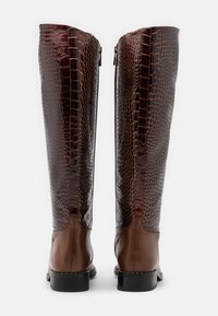 Bottes montantes en cuir marron avec un panneau marron foncé à motif crocodile, une fermeture éclair à l'arrière et un petit talon noir.