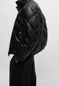 Giacca trapuntata nera in materiale lucido, con colletto alto e tasche laterali con zip, elastici sui polsini e sull'orlo.