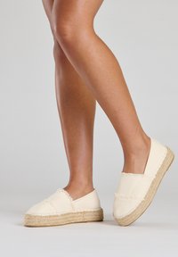 Leinen-Espadrilles in Creme mit fransigen Kanten, Jutesohlen und einem Slip-On-Design, das eine abgerundete Zehenform und eine leichte Konstruktion zeigt.