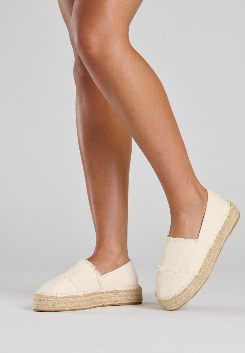 Leinen-Espadrilles in Creme mit fransigen Kanten, Jutesohlen und einem Slip-On-Design, das eine abgerundete Zehenform und eine leichte Konstruktion zeigt.