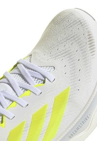 Close-up of white and neon yellow athletic shoe with mesh upper, white laces, and "Dreamstrike" text on the sole.