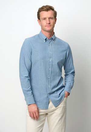 Hellblaues Button-Up-Hemd aus weichem Stoff, mit klassischem Kragen, langen Ärmeln und leicht abgerundetem Saum; getragen mit cremefarbenen Hosen.