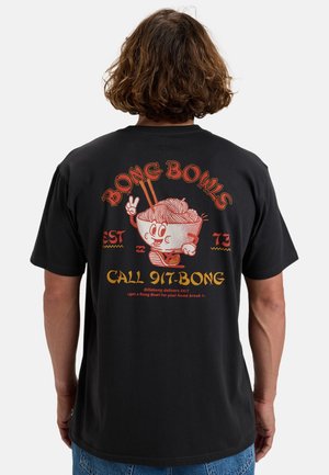 Osoba w czarnej koszulce z nadrukiem kreskówkowej miski z makaronem trzymająca pałeczki i pokazująca znak pokoju, z napisem "Bong Bowls" i numerem telefonu na plecach.