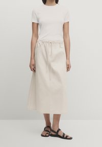 Beige, knælang nederdel lavet af bomuld, med en elastisk talje med snøring, sidelommer og et minimalistisk design.