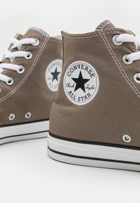 Brązowe płótniowe trampki za kostkę z białymi sznurówkami, czarnym logo gwiazdy oraz gumową podeszwą z czarno-białymi paskami.