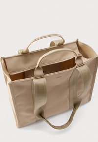 Beżowa torba na ramię z płótna z dwoma górnymi uchwytami, zamkiem błyskawicznym i przestronnym wnętrzem. Charakteryzuje się teksturowanymi paskami oraz subtelnym logo.