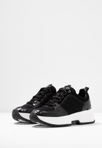 Sneaker nere con dettagli in pelle verniciata e texture, dotate di suola e lacci bianchi, superficie testurizzata e design chunky moderno.