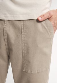 Khaki katoenen broek met zijzakken, een relaxte pasvorm en zichtbare stiksels. De stof heeft een zachte, gestructureerde uitstraling.