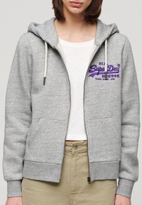 Felpa grigia con zip, realizzata in misto cotone, con cappuccio regolabile, tasche a marsupio e logo ricamato viola sul petto.