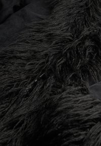 Sorte faux fur med lange, teksturerede fibre, lagd over en glat sort stof. Rigt detaljere og blødt at røre ved.