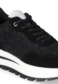 Sneakers neri con una combinazione di tessuto testurizzato e suede, caratterizzati da un design laterale a fantasia, una suola intermedia bianca e una suola esterna in gomma nera.