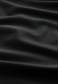 Czarna tkanina z delikatnym wzorem kratki, ukazana z bliska z miękkimi fałdami i widoczną teksturą pod przyćmionym oświetleniem.