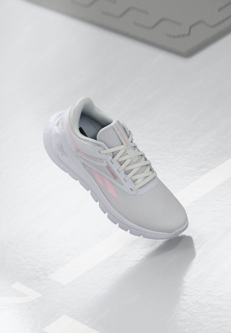 Lysgammel atletiksko med pink detaljer, meshoverdel, rund tå, polstret sål og snørelukning. Overfladen er glat og reflekterende.