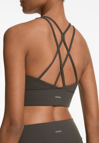 Donkergrijze sportbeha met een crisscross strapdesign aan de achterkant en een logo-detail nabij de zoom, gemaakt van een gladde, rekbare stof.