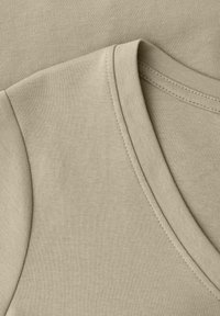 Gros plan sur un tissu en coton beige montrant des coutures détaillées et un col en V plié d'un vêtement, mettant en évidence la texture et la qualité des coutures.