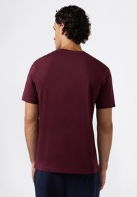 Maglietta a maniche corte di colore bordeaux in cotone morbido, con colletto rotondo e vestibilità standard, caratterizzata da una texture liscia e senza motivi visibili.