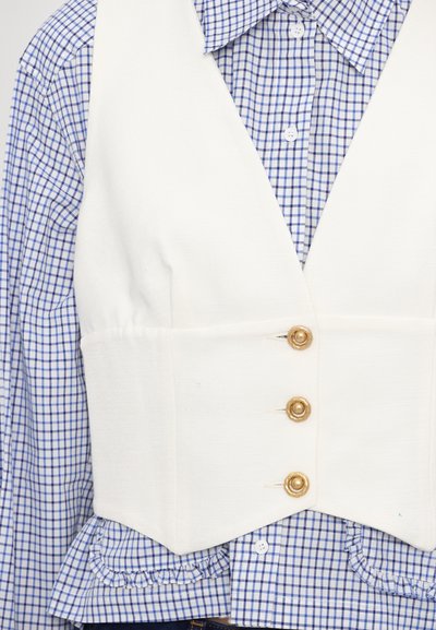 Hvit vest med en strukturert design, prydet med tre gullknapper foran, lagdelt over en blå og hvit rutete skjorte med volanger.