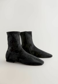 Sorte ruskind ankelstøvler med spidse tæer, der har en sidelukning og glat tekstur, designet til at sidde tæt omkring anklen.
