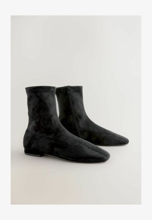 Czarne zamszowe botki za kostkę z ostrym noskiem, z bocznym zamkiem błyskawicznym i gładką fakturą, zaprojektowane do ścisłego przylegania wokół kostki.