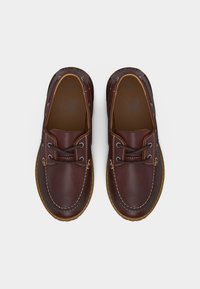 Ζευγάρι σκούρα καφέ δερμάτινα casual παπούτσια τύπου boat με ραφές και κορδόνια, σε θέα από πάνω σε λευκό φόντο.