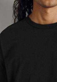 Černé bavlněné tričko s kulatým výstřihem a krátkými rukávy, s hladkou texturou a minimálními designovými detaily.