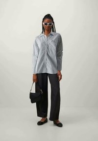 Striped button-up shirt in blue and white, black wide-leg trousers, black flats, and a small black handbag. White sunglasses as an accessory.