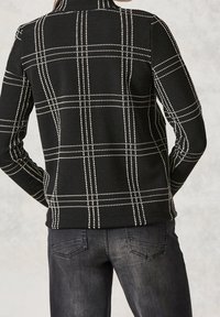 Black jacket with a textured fabric featuring a white plaid pattern. Stand-up collar, long sleeves, and fitted design.
