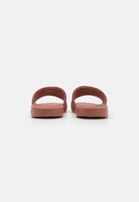 Infradito in gomma marrone con apertura sul retro e un design fluido e curvo. Presentano una soletta imbottita e nessuna hardware visibile.